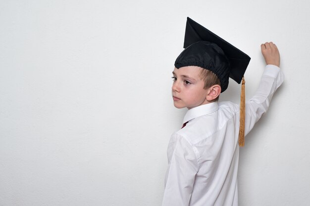 Chłopiec w studenckim kapeluszu pisze na blackboard. Biała ściana kopia przestrzeń. Koncepcja edukacji