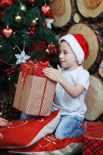 Chłopiec w świątecznych czapkach siedzi z prezentami w dłoniach z radością niespodzianki.