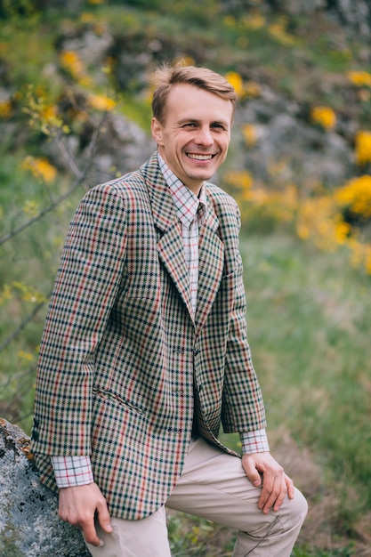 Chłopiec w szkockiej kraty kurtce pozuje przed skałami i żółtymi kwiatami