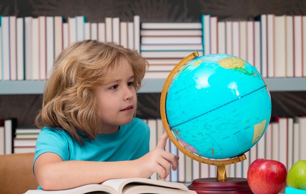 Chłopiec w szkole patrząc na kulę ziemską na lekcji geografii w bibliotece Dziecko w wieku szkolnym uczeń uczący się w klasie uczy się języka angielskiego w szkole Dziecko w szkole podstawowej Portret śmiesznego ucznia uczącego się