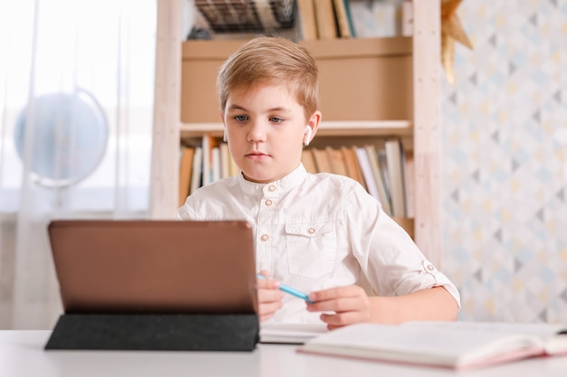 Chłopiec w szkole robi swoje zadanie w domu przy użyciu komputera typu tablet i podręczników