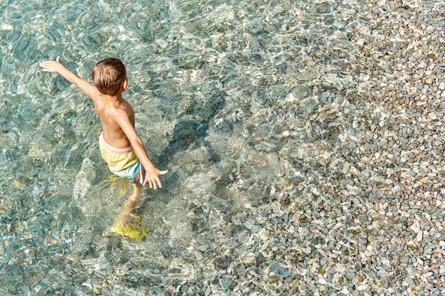 Chłopiec w wieku przedszkolnym lubi odkrywać wodę morską na nasłonecznionej plaży Kid chodzi po morzu żwirowym