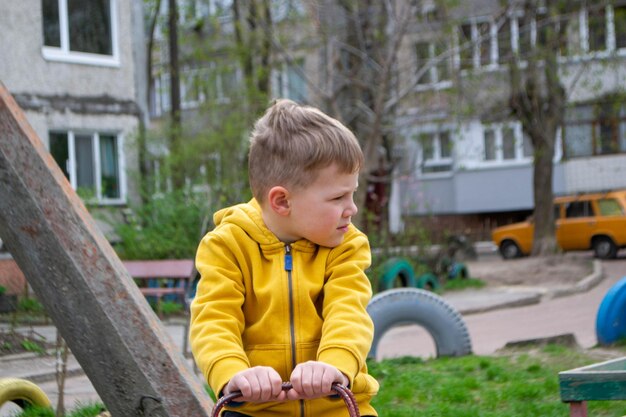 Chłopiec w żółtej kurtce siedzi na pniu drzewa.