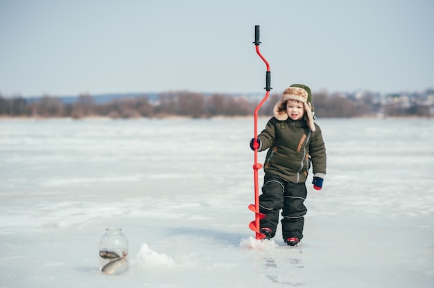 Chłopiec wędkowanie na zimę. Ładny chłopak łapie ryby w jeziorze zimą. Zimowy. Na wolnym powietrzu