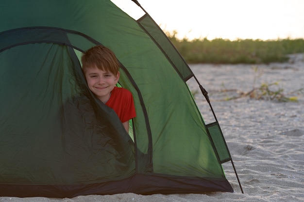 Chłopiec wyglądający z namiotu turystycznego. Aktywne wakacje. Kemping.