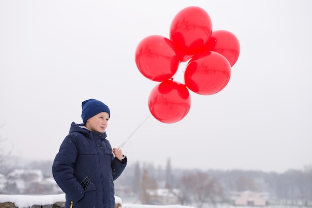 Zdjęcie chłopiec z czerwonymi balonami w zimie na zewnątrz