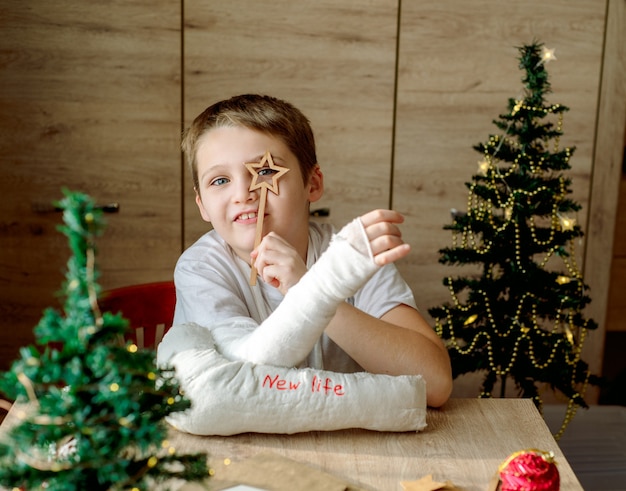 Chłopiec z gipsem na ramieniu robi świąteczne rękodzieło. Złamanie i uraz ręki. Usuwa odlew gipsowy