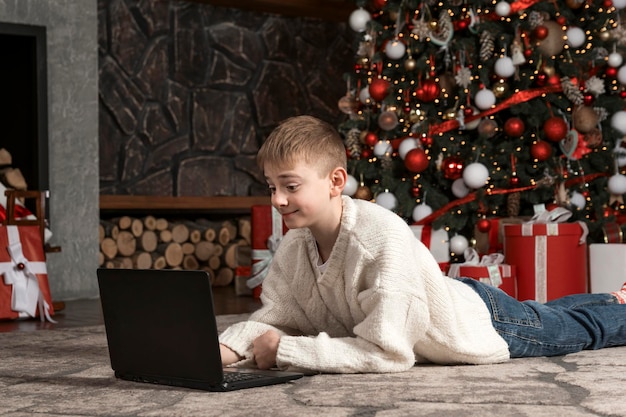 Chłopiec z laptopem przy choince Dziecko otrzymało laptop jako prezent na Nowy Rok Nastolatka oglądała bożonarodzeniowe filmy