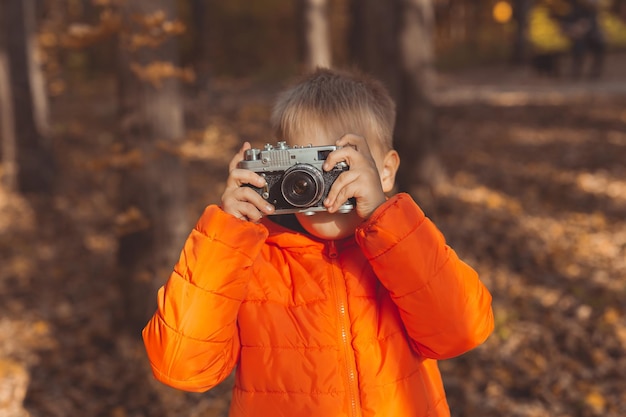 Chłopiec z retro aparatem robi zdjęcia plenerowy w jesiennej przyrodzie. Koncepcja wypoczynku i fotografów