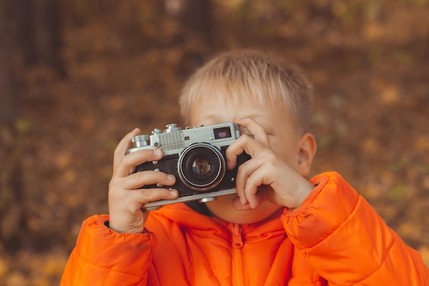 Chłopiec z retro aparatem robi zdjęcia plenerowy w jesiennej przyrodzie. Koncepcja wypoczynku i fotografów