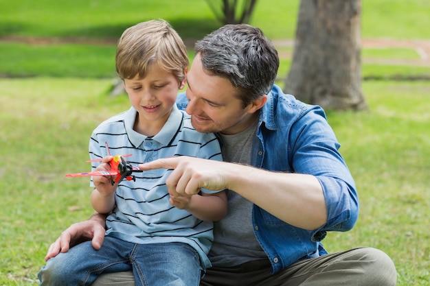 Chłopiec z zabawkarskim samolotowym obsiadaniem na ojca podołku przy parkiem