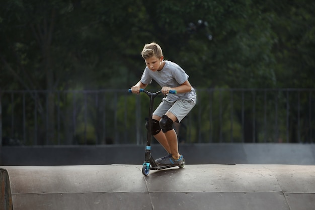 Zdjęcie chłopiec ze skuterem leci w powietrze w skateparku