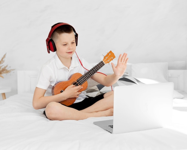 Zdjęcie chłopiec ze słuchawkami, grając na ukulele i ucząc się online