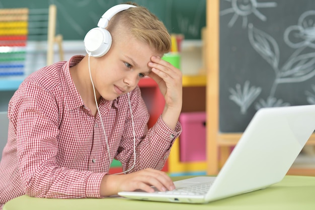 Chłopiec ze słuchawkami używający laptopa w klasie