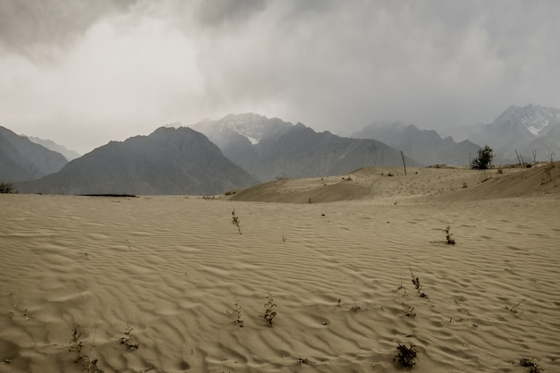 Chmurna i zakurzona scena po burzy w Katpana pustyni z śniegiem nakrywał góry w karakoram pasmie, Pakistan.