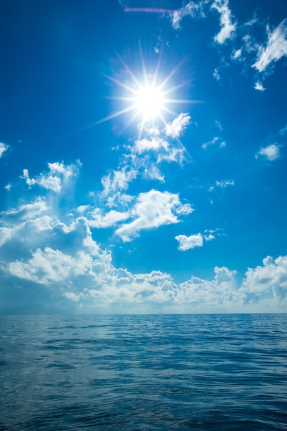 Chmury na niebieskim niebie nad spokojnym morzem z odbiciem światła słonecznego