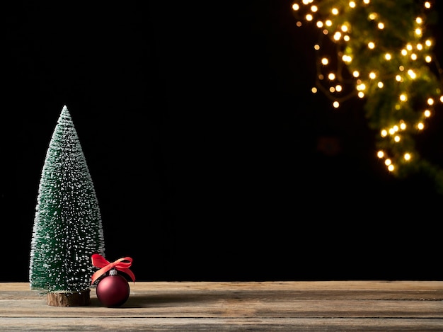 Choinka i czerwone kulki na drewnianym stole przed niewyraźne świąteczne światła. Miejsce na tekst