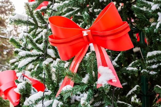 Choinka na śniegu z dużą czerwoną kokardą i rozmytym tłem Koncepcja dekoracji ulicznych miasta na Boże Narodzenie