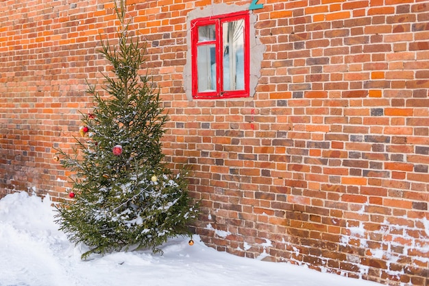 Choinka ozdobiona świecącymi światłami i kulkami i girlandami noworocznymi na zewnątrz choinki przed budynkiem na ulicy