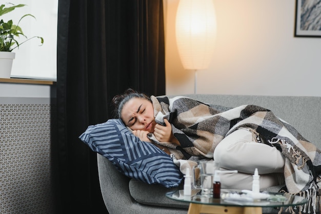 Chora kobieta GrypaKobieta złapana przeziębieniem przez kichanie w tkankę Wirus na ból głowy Leki Chora kobieta z bólem głowy siedząca na kanapie