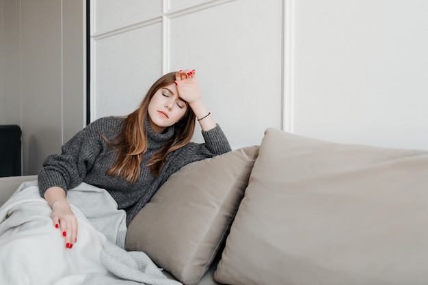Chora kobieta z bólem głowy na kanapie w domu dotykając jej czoła w poszukiwaniu gorączki