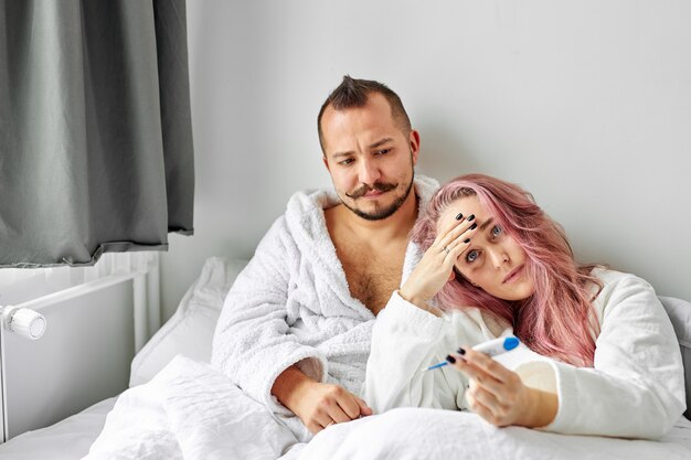Chora kobieta z mężem na łóżku, kobieta ma wysoką temperaturę, gorączkę. w sypialni