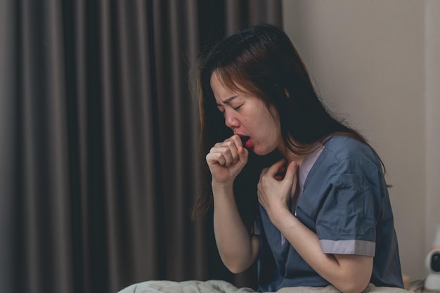 chora młoda kobieta siedzi w łóżku i kaszle podczas bólu gardła
