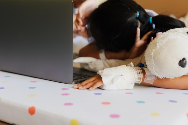 Chore azjatyckie dziecko czuje się znudzone i leży na łóżku podczas nauki online z nauczycielem i przyjacielem podczas pobytu w prywatnych pokojach pacjentów w szpitalu. Nauczanie domowe w izolacji i nauczanie na odległość.