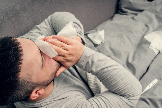 Choroba. Dopinguj w domu. Młody mężczyzna jest chory, leczony w domu. Dmucha jej nos w serwetkę, katar. Zakażenie, epidemia, nosiciel Bacillus.