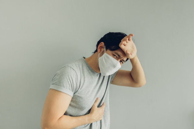 Chory mężczyzna nosi białą higieniczną maskę w szarej koszulce w koncepcji wirusa.