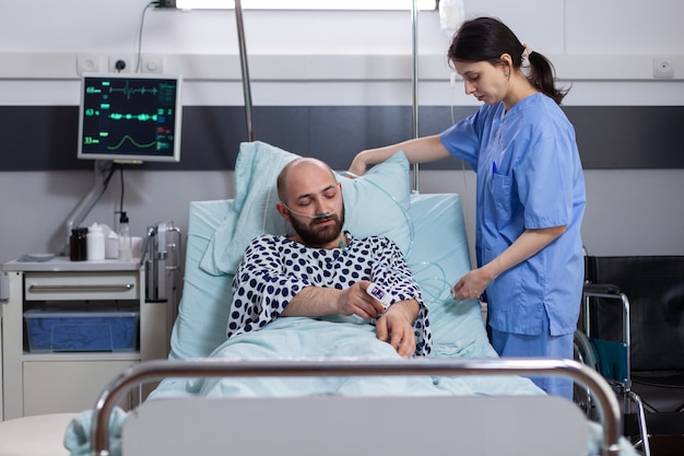 Chory mężczyzna odpoczywa w łóżku, podczas gdy pielęgniarka układa łóżko, aby wygodnie usiąść