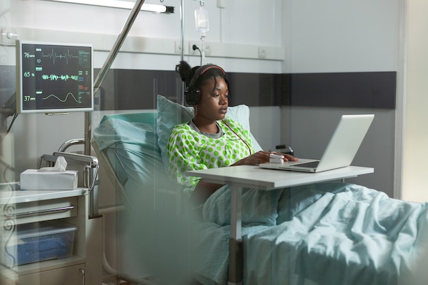 Chory młody pacjent ze słuchawkami używający laptopa