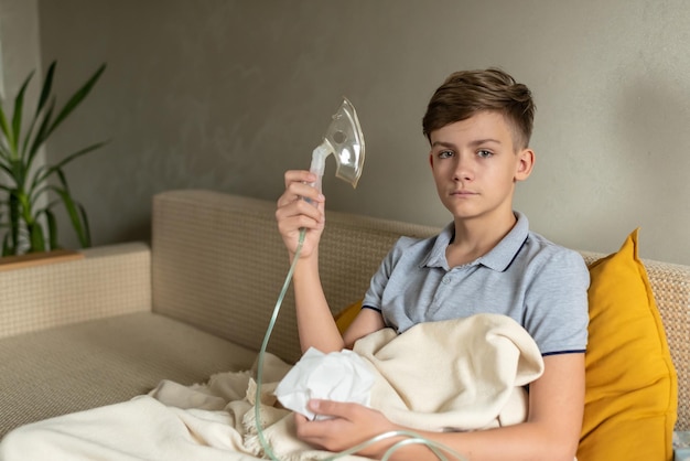 Chory nastolatek z inhalatorem Niezdrowe dziecko robiące inhalację w domu używa do leczenia nebulizatora i inhalatora siedząc na kanapie w domu Astma inhalator nebulizator para grypa lub przeziębienie
