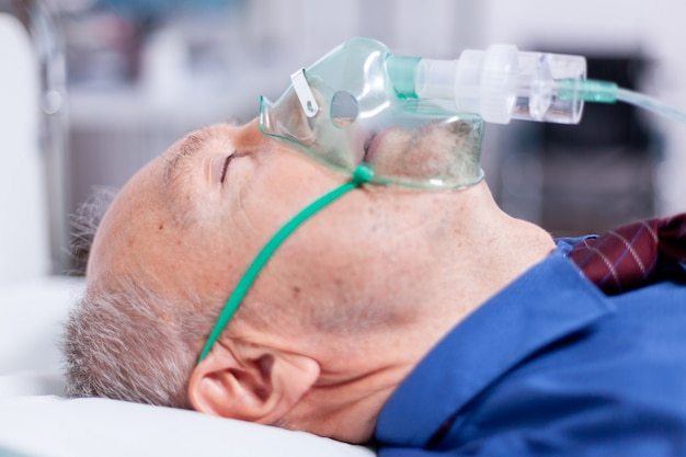 Zdjęcie chory starzec z maską oddechową leżący na szpitalnym łóżku po zarażeniu koronawirusem