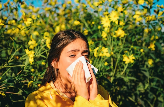 Chrapająca młoda dziewczyna z wycieraczką do nosa wśród kwitnących kwiatów w parku młoda kobieta dostała alergii na grypę z nosa