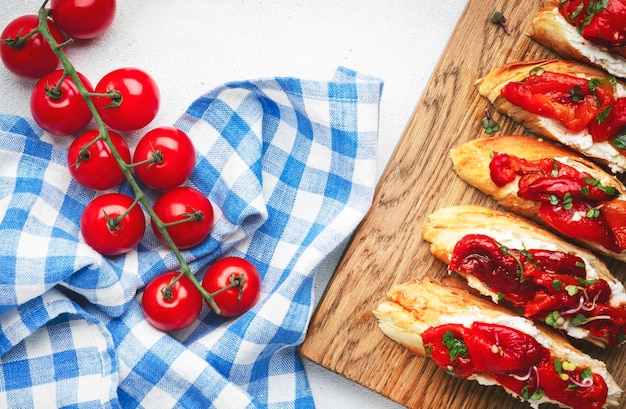 Chrupiąca bruschetta z miękkim kozim serem i słodką czerwoną papryką w oliwie z oliwek z ziołami na desce do krojenia na białym stole kuchennym tle widok z góry