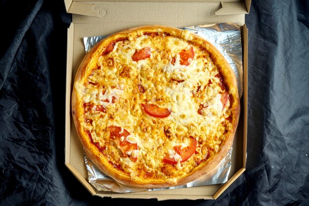Chrupiąca włoska pizza z pomidorami i roztopioną mozzarellą w dostawie na czarnym stole. Widok z góry. Pizza Margarita z piekarnika