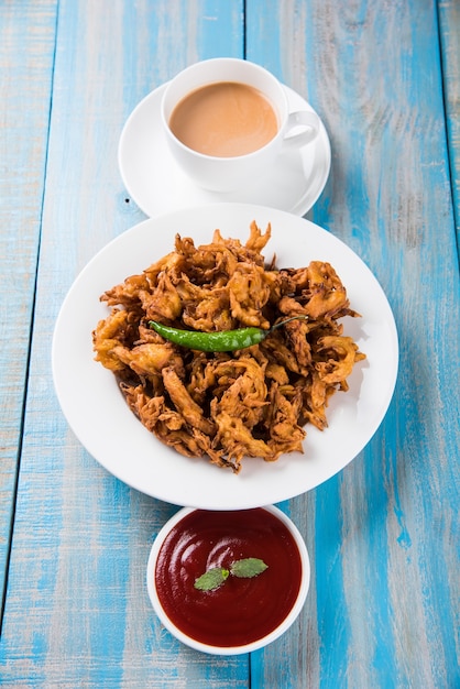 Chrupiące Kanda bhaji lub Bhajji lub Pyaj Pakode lub smażona cebulowa pakora, pyszne jedzenie uliczne, ulubiona indyjska przekąska w monsunie podawana z ketchupem pomidorowym i gorącą herbatą