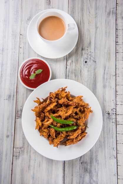 Chrupiące Kanda bhaji lub Bhajji lub Pyaj Pakode lub smażona cebulowa pakora, pyszne jedzenie uliczne, ulubiona indyjska przekąska w monsunie podawana z ketchupem pomidorowym i gorącą herbatą