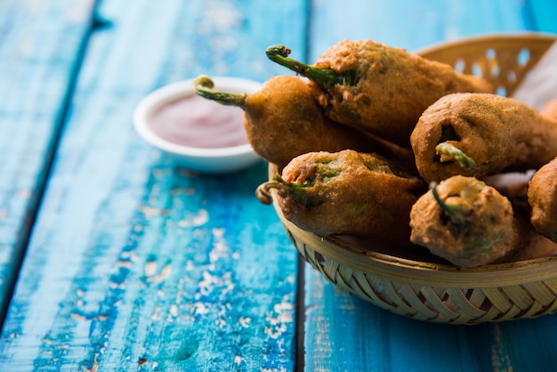 Chrupiące zielone Chilli Pakora lub Mirchi Bajji, podawane z ketchupem na nastrojowym tle. Jest to popularna przekąska na herbatę z Indii, szczególnie w Monsoon. Selektywne skupienie