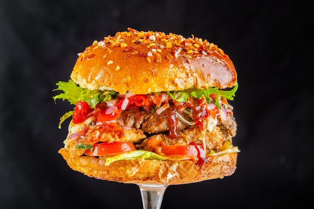 Zdjęcie chrupiący burger z chrupiącego chleba, sos pomidorowy, ser, krążki cebulowe, warzywa, na czarnym tle