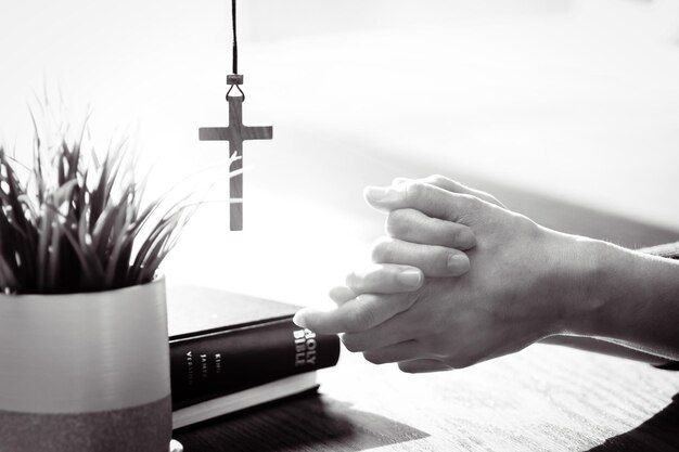 Zdjęcie chrześcijanie modlą się i oddają cześć rękami razem jasno oświetloną biblią i krzyżem w tle