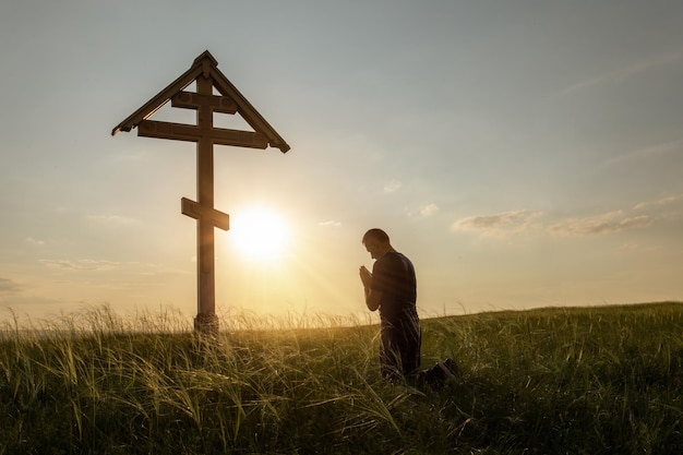 Zdjęcie chrześcijanin modlący się na łące o zachodzie słońca człowiek modlitwy na zewnątrz modlitwa pod krzyżem