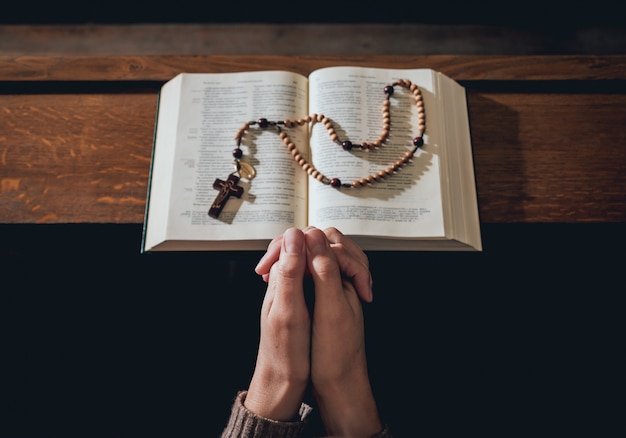 Chrześcijańska Kobieta Modli Się W Kościele. Ręce Skrzyżowane I Pismo święte Na Drewniane Biurko.