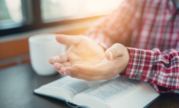 Chrześcijańska ręka modląc się i oddając cześć religii chrześcijańskiej z rozmytym tłem jej ciała, przypadkowy mężczyzna modlący się ze złożonymi rękami nad zamkniętą Biblią. chrześcijańskie tło. wolność.