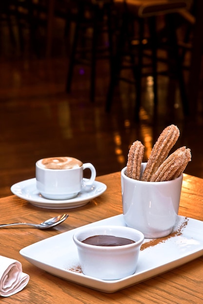 churros z czekoladą do maczania i kawa cappuccino na drewnianym stole w restauracji deser