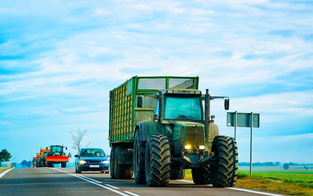 Ciągnik rolniczy z przyczepą w drodze. Furgonetka pojazdu rolniczego w pracy na podjeździe. Transport europejski. Transport wiejski na autostradzie.