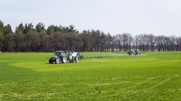 Ciągnik rozpylający środek owadobójczy na zielonym polu rolniczym naturalnym sezonowym wiosennym tle