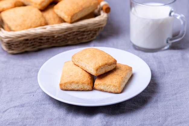 Ciasteczka na białym talerzu. koszyk ciastek i kubek mleka. Zbliżenie.