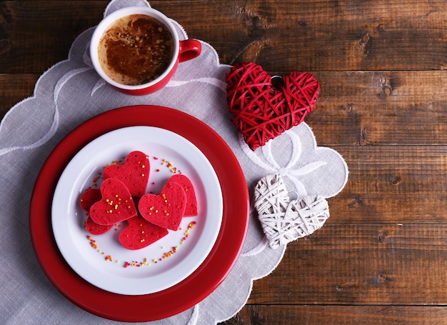 Ciasteczka w formie serca w talerzu z filiżanką kawy na serwetce, na tle rustykalnych drewnianych desek